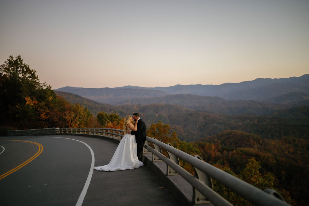 foothills parkway elopement with bride and groom embracing on the road with groom leaning against the railing of the parkway