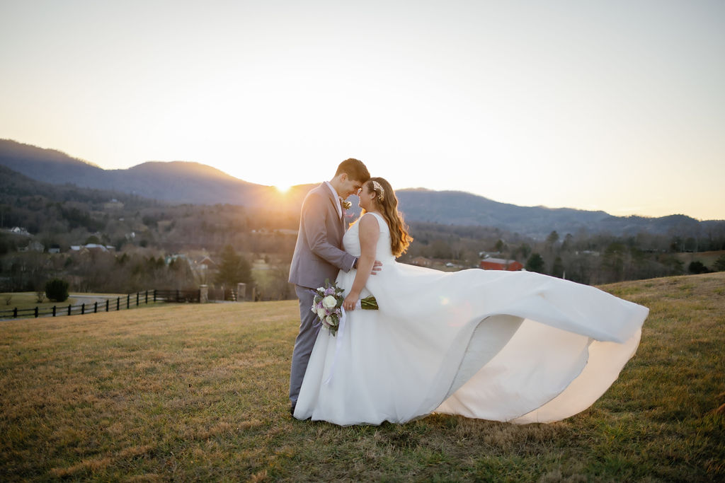 Gatlinburg wedding photographer captures elopement at Harpers Vineyard with bride and groom embracing on a hill at sunset with the brides gown blowing in the wind behind her