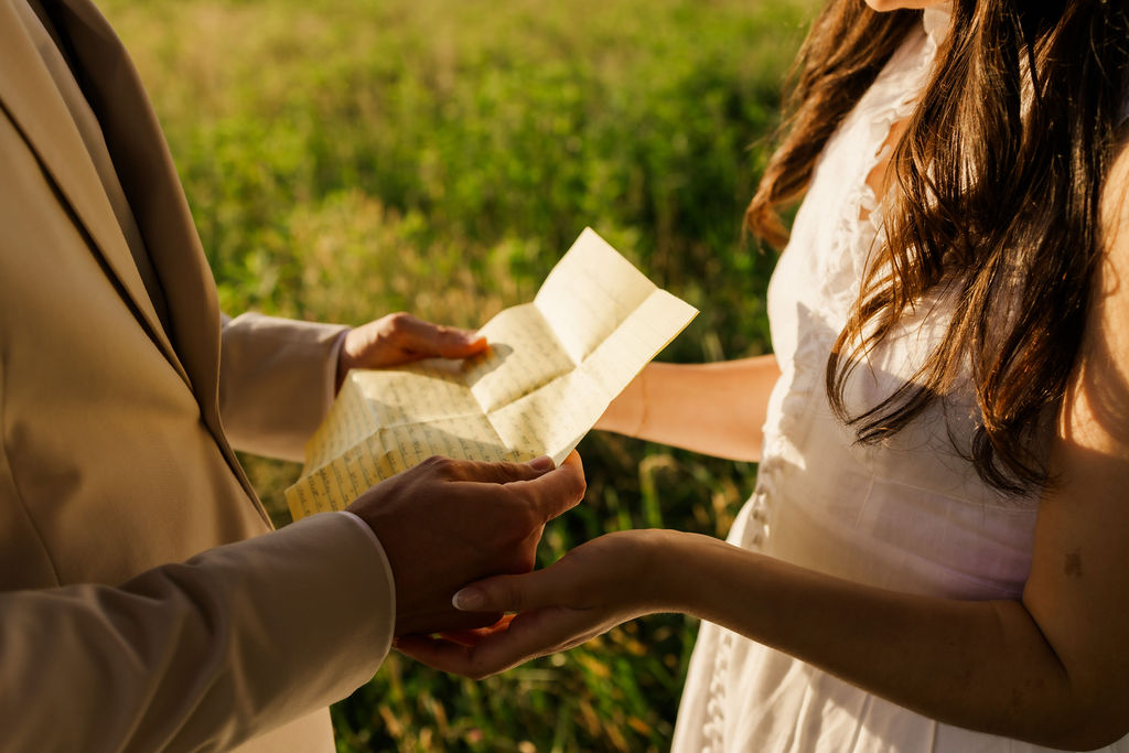 groom holding his vows as his bride holds his hands gently