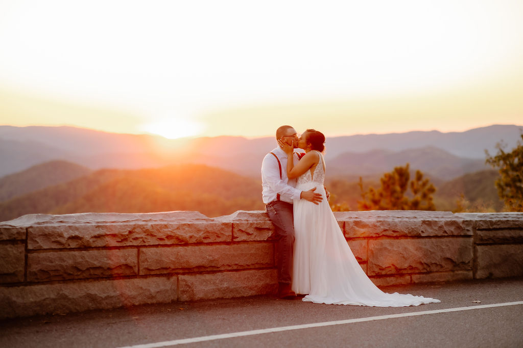 sunset wedding picture by Gatlinburg elopement photographer with couples embracing on the foothills parkway and kissing passionately as a bright red and pink sunset shines behind them