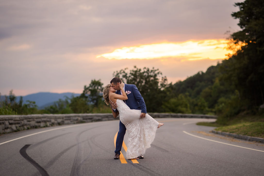 photographers in gatlinburg tn captures sunset wedding picture with groom dipping his bride backwards and kissing her passionately in the middle of the road at the foothills parkway